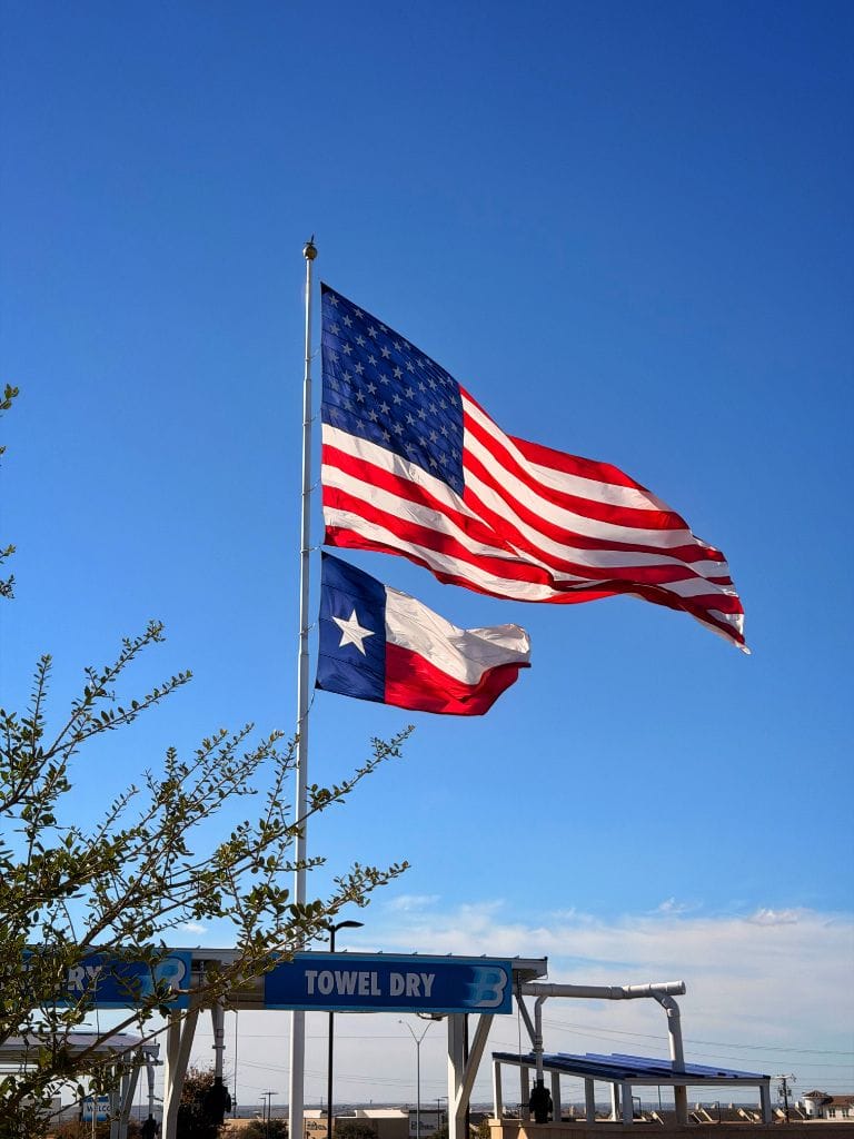 American and Texas flags flying proudly against a vivid blue sky above the Brightworks Fort Worth towel-dry station
