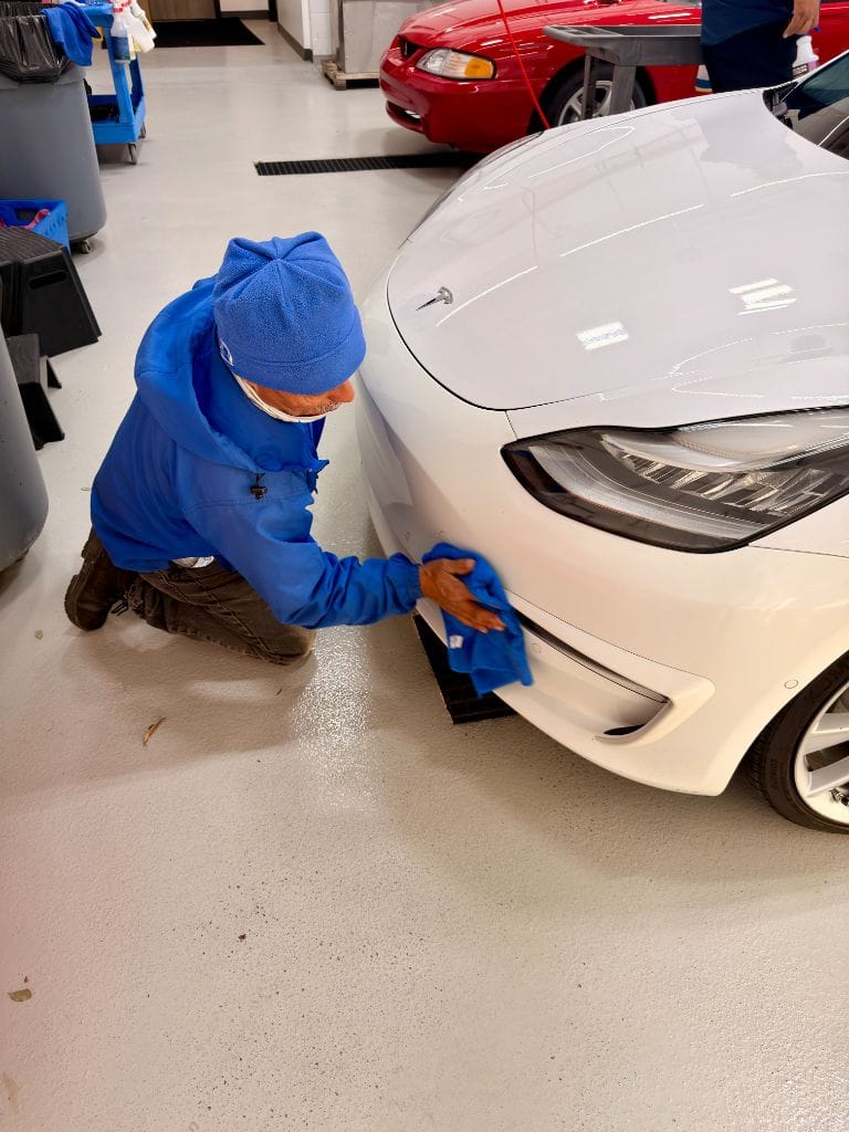 Brightworks Fort Worth team member kneeling to hand-polish the front bumper of a white Tesla Model 3 in the detail bay