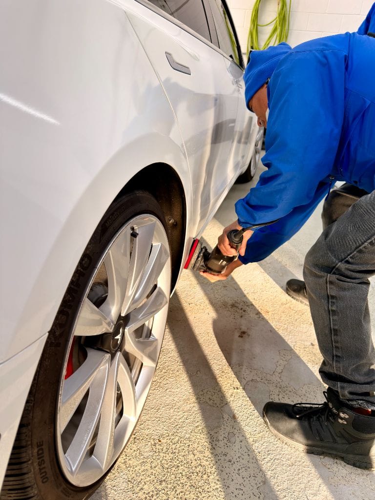 Brightworks Fort Worth detailer using a power tool to clean the rocker panel and wheel arch of a white Tesla Model 3