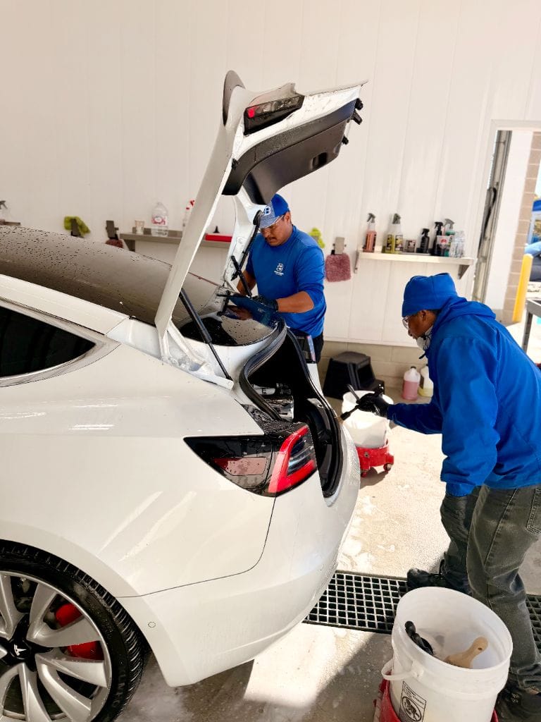 Two Brightworks Fort Worth team members in blue uniforms detailing the trunk and rear of a white Tesla Model 3