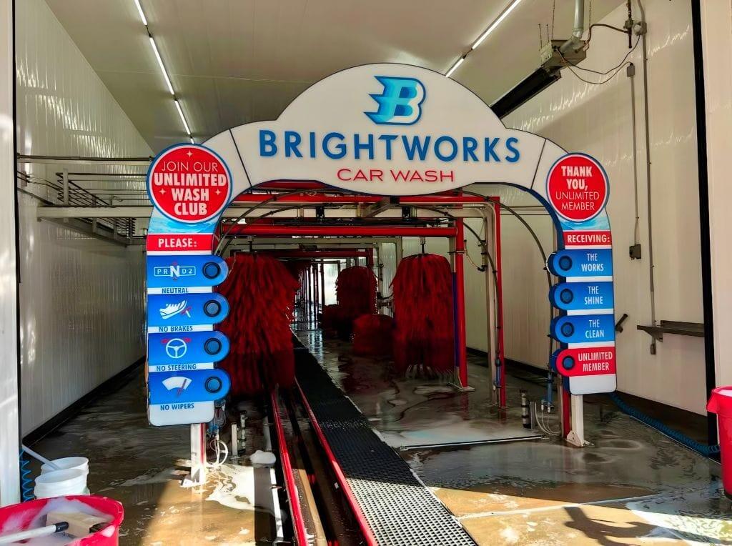 Brightworks Car Wash branded entry arch at Fort Worth showing wash menu, Monthly Wash Club and red brushes inside the exterior wash