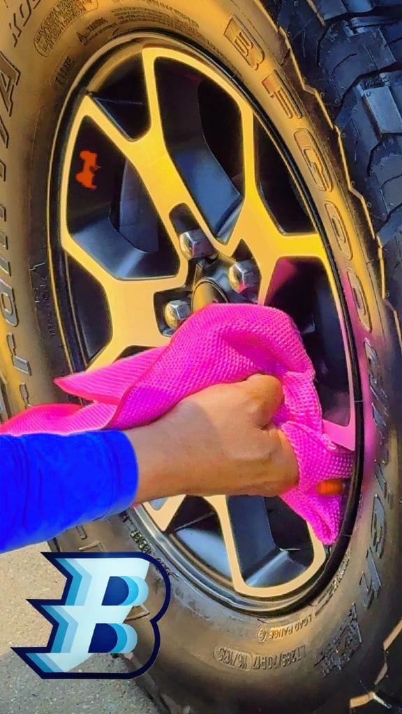 Brightworks team member polishing a gold truck wheel with a pink microfiber cloth
